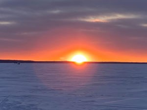 An image of a sunset behind ice huts on frozen Lake Nipissing